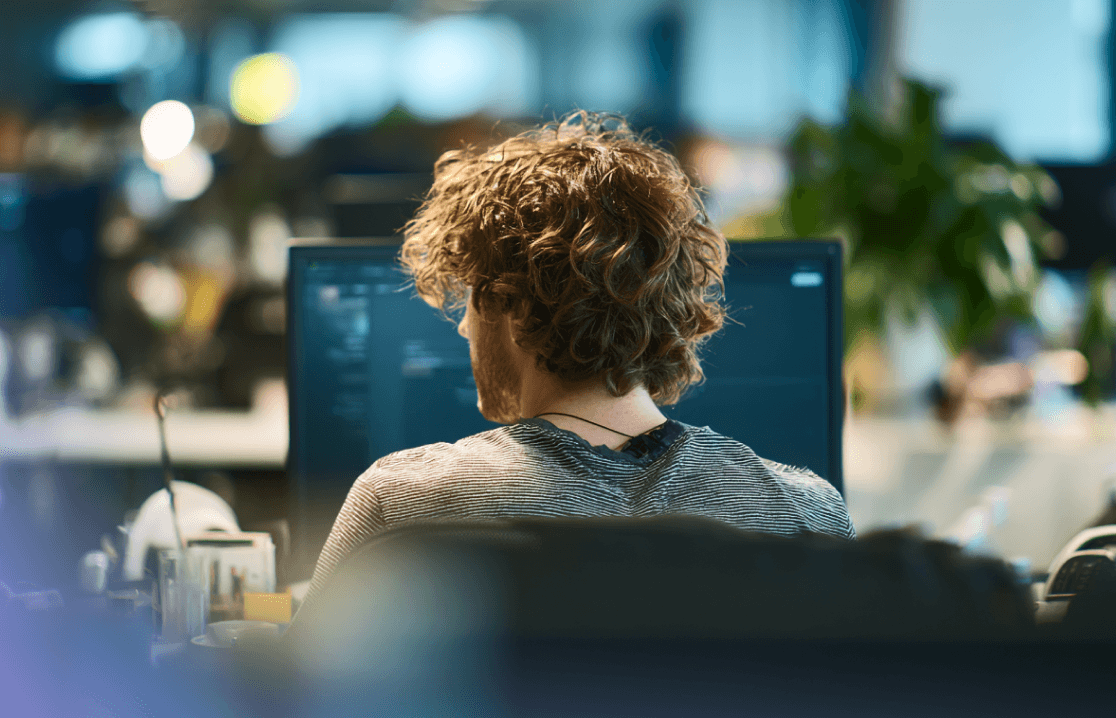 Set over skulderen på en udvikler med krøllet hår, der arbejder på en computer på et moderne kontor.